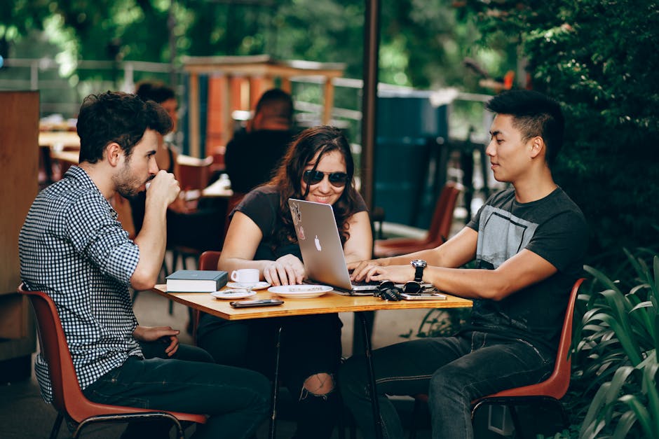 A group of young adults working on a laptop at an outdoor coffee shop, enjoying teamwork and collaboration.
